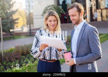 Mature businessman discussing work with his female colleague outdoors. Two business coworkers examining documents in front of business building Stock Photo