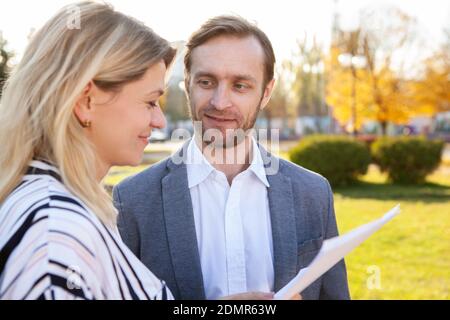 Mature businessman smiling at his female colleagues, while talking outdoors. Business colleagues talking outside on a warm autumn day Stock Photo