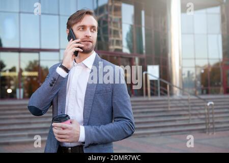 Mature businessman talking on the phone, having coffee outdoors. Confident male entrepreneur using smart phone during coffee break from work Stock Photo