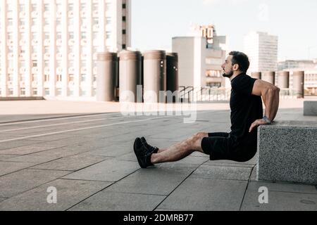 Fit man pushing from stone cube. Morning workout outdoors. Black sportswear. Man practicing hard to strengthen his arms. Urban sport concept. Morning Stock Photo