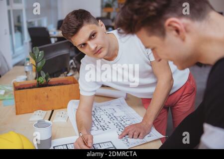 Architects office, building construction concept. Handsome male engineer working on a building sketch with his colleague Stock Photo