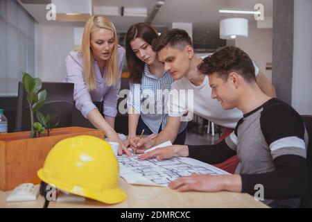 Group of young architects examining architectural blueprints together, copy space. Professional engineers working on a building plan at the office. Te Stock Photo