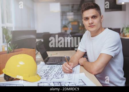 Inspiration, project concept. Attractive young male architect looking to the camera confidently, working on blueprints at his office, copy space Stock Photo