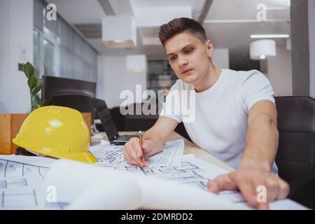 Business, real estate concept. Attractive young male engineer drawing building plan sketches at his office, examining blueprints Stock Photo