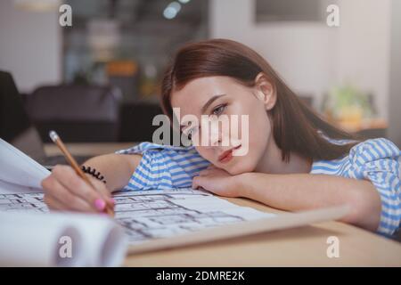 Close up of a charming young female architect working on a building plan. Attractive female engineer drawing on a blueprint, enjoying working on her p Stock Photo