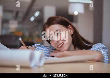 Close up of a happy beautiful female entrepreneur smiling, working on a business project at her office, copy space. CHarming young female engineer enj Stock Photo
