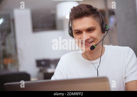 Handsome young man smiling, playing video games on computer, wearing headset. Male gamer enjoying playing and streaming walkthrough, playing video gam Stock Photo