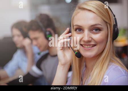 Close up of a happy beautiful young woman enjoying working at customer support call center. Attractive female customer services operator wearing heads Stock Photo