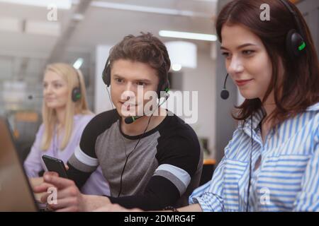 Group of young people working at customer services call center. Handsome male call center operator talking to his colleague while working. Client serv Stock Photo