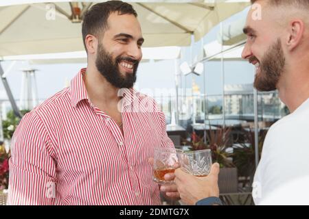 Handsome bearded man laughing, enjoying drinks with his friends on a summer party Stock Photo