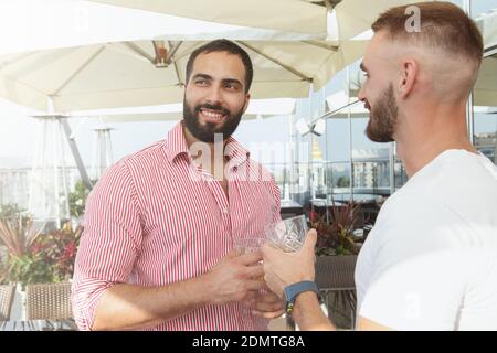 Attractive bearded man drinking whiskey with his friend on a rooftop party Stock Photo