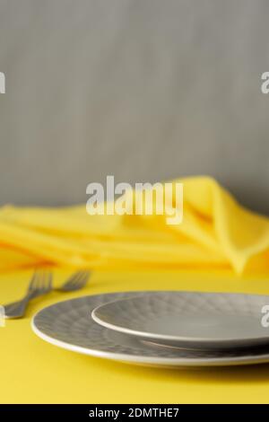 Table setting in trendy colors of the year, gray plates and a fork with a spoon on a yellow background with a yellow tablecloth Stock Photo