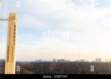 outdoor thermometer on home window lit by dawn sun in cold winter morning and blurred forest and residential district on horizon (focus on the thermom Stock Photo