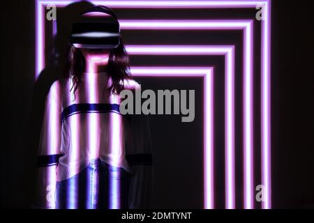 Woman using virtual reality headset, moving hand at interactive technology exhibition with multicolor projector light illumination, immersive concept Stock Photo