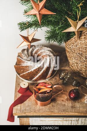 Cup of mulled wine and Christmas bundt cake over wooden kitchen counter with festive decorative baubles and stars and Christmas tree branches at background. Winter holiday mood concept Stock Photo