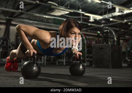 Life of fitness. Attractive young gym fitness woman doing pushups with weights beautiful sportswoman doing crossfit workout pushups exercise with kett Stock Photo