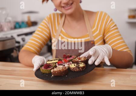 Cropped shot of a female confectioner putting delicious raw vegan tarts on a plate, working at her confectionery store Stock Photo