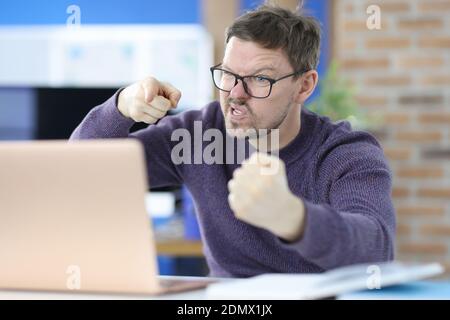 Angry man sits at work table in front of laptop Stock Photo