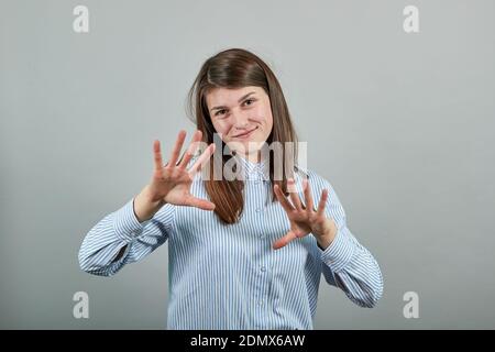 Claw hands, hand gesture and sign, scary desperate, showing claws, nails, making silly face. Young attractive woman, dressed blue shirt with brown eyes, brunette hair, grey background Stock Photo