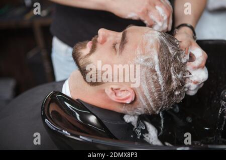 Close up of a bearded man relaxing while barber washes his hair with shampoo Stock Photo
