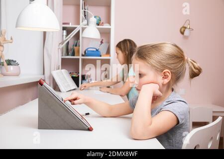 Girls sitting by the desk in the children's room studying at home doing homework during Coronavirus COVID-19 quarantine Stock Photo