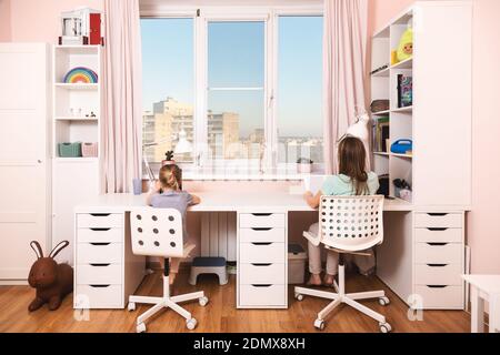 Girls sitting by the desk in the children's room studying at home doing homework during coronavirus COVID-19 quarantine Stock Photo