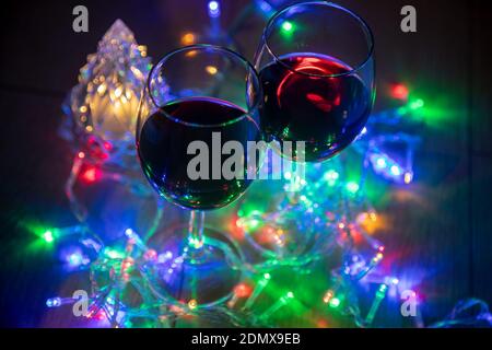 two glasses on the background of a shining Christmas tree and a multi-colored garland on a dark night background. New Year celebration... Stock Photo