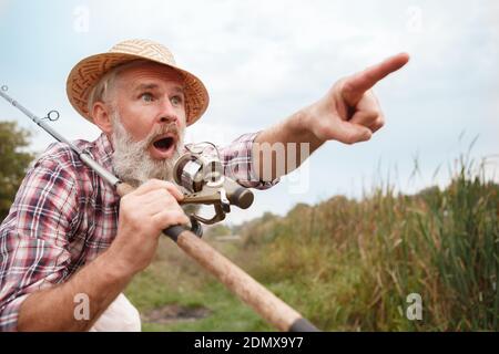 Shocked senior fisherman pointing away with his mouth open in shock Stock Photo