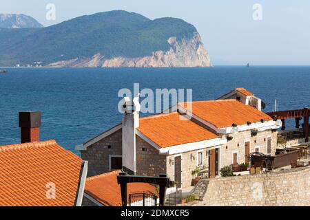 Petrovac, Budva, Montenegro. View over the tiled roofs of a café restaurant on the Venetian fortress, the Adriatic Sea beyond. Stock Photo