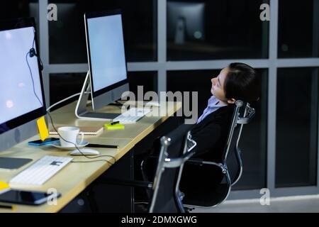 Asleep exhausted Asian lady call center worker employee sleeping on dest at night tired from late working alone in office. Ider for suffering and hard Stock Photo