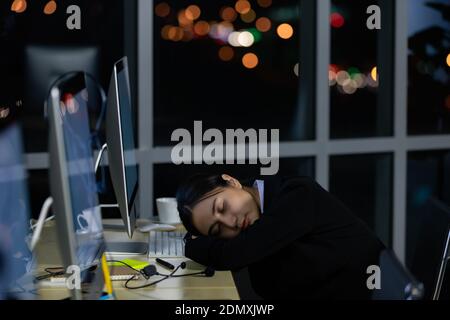 Asleep exhausted Asian lady call center worker employee sleeping on dest at night tired from late working alone in office. Ider for suffering and hard Stock Photo
