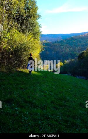Rear of a woman, wearing dress and shawl, standing alone on a slope taking in the beautiful view of the Cevennes mountains in france, on an autumn day Stock Photo