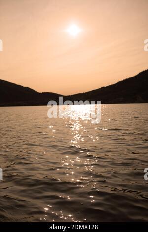 a peaceful view over a lake late afternoon with the sun's reflections glistening on the water's surface Stock Photo