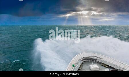 Lindblad's MS National Geographic Explorer in heavy waves in the off the coast of Svalbard with sun beams (God rays or Crepuscular rays) in distance. Stock Photo