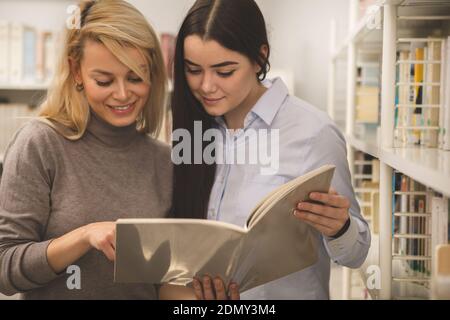 Two college students enjoying working on a project together, reading a book at campus library. Lovely female friends studying at the university. Beaut Stock Photo
