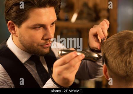 Close up of a handsome professional barber looking focused and concentrated giving a haircut to his client profession occupation job work fashion hair Stock Photo
