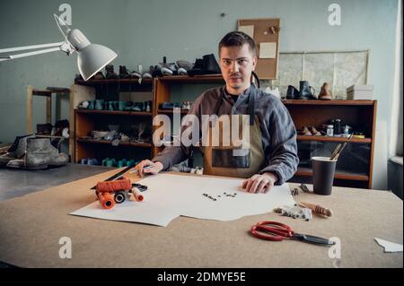 In a family shoe shop a young apprentice works with paper to create a pattern for shoes. Stock Photo