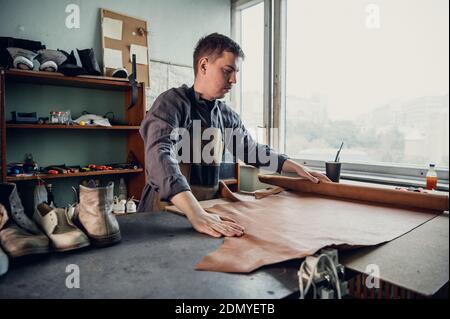 Experienced specialist in the production of footwear leather lays on a table in his workshop. Stock Photo
