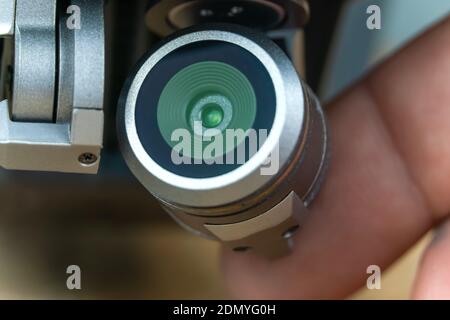 Camera of a gray quadrocopter close-up standing on a table. Male fingers hold the drone's camera. Stock Photo
