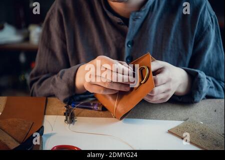 A young shoemaker manually sews decorative elements to leather shoes in the workshop. Stock Photo