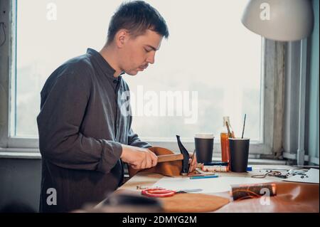 In a shoe workshop, a tanner makes handmade shoes using a hammer and other tools. Stock Photo