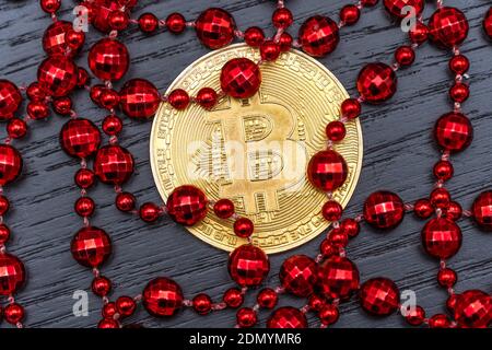 Gold coin bitcoin lies on a dark background among red beads close-up, top view. Stock Photo