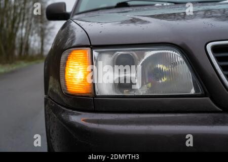 Close-up of the right headlight of a gray car with the emergency light on. Stock Photo