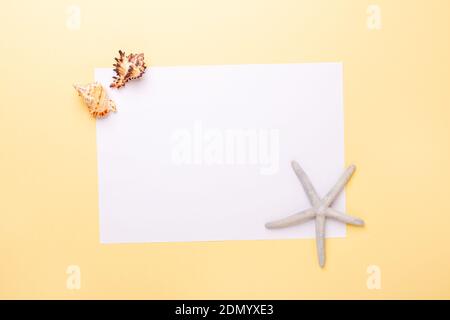 Blank paper, seashells and starfish on yellow background. Concept of planning summer holidays and vacation - Image Stock Photo