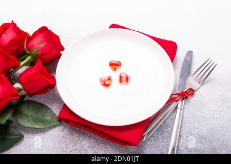 Valentines day table place setting with bouquet of roses, red hearts and silverware on stone background. Valentine's card. - Image Stock Photo