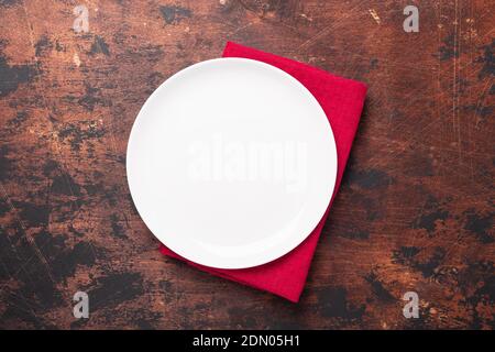Empty ceramic white plate and red linen napkin on brown wooden background Copy space Top view - Image Stock Photo