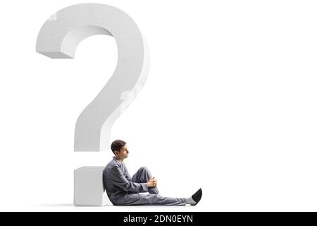 Pensive man in pajamas sitting on the floor and leaning on a question mark isolated on white background Stock Photo