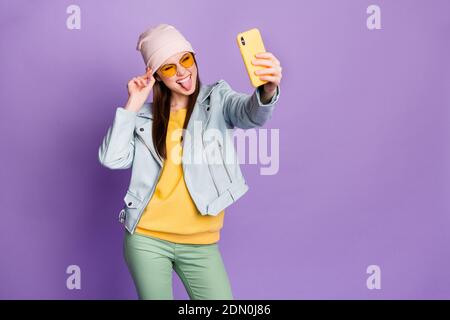 Photo of stylish pretty lady hold telephone smiling showing tongue make selfies followers blogger wear sun specs casual hat blue jacket pullover green Stock Photo