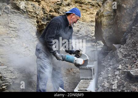 Elderly worker cutting concrete blocks with radial, during the construction of a wall. Stock Photo