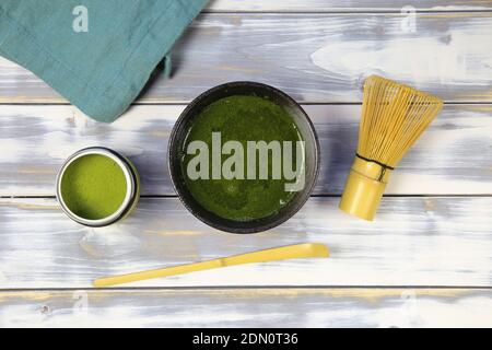 Top down view on white wood table with chawan bowl, bamboo whisk and spoon, can green matcha tea powder and blue napkin Stock Photo
